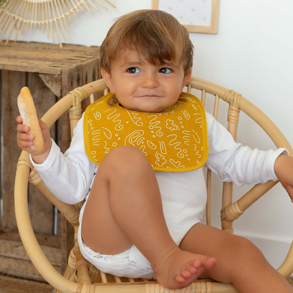 Bébé qui mange son bouvoir avec son bavoir moutarde Bébé qui mange son bouvoir avec son bavoir moutarde