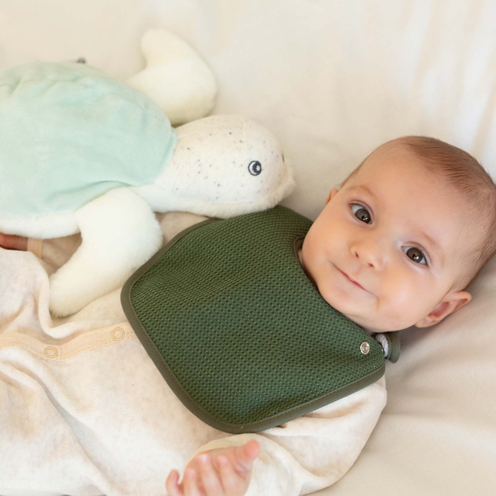 Bébé avec son bavoir olive et sa peluche la tortue Bébé avec son bavoir olive et sa peluche la tortue
