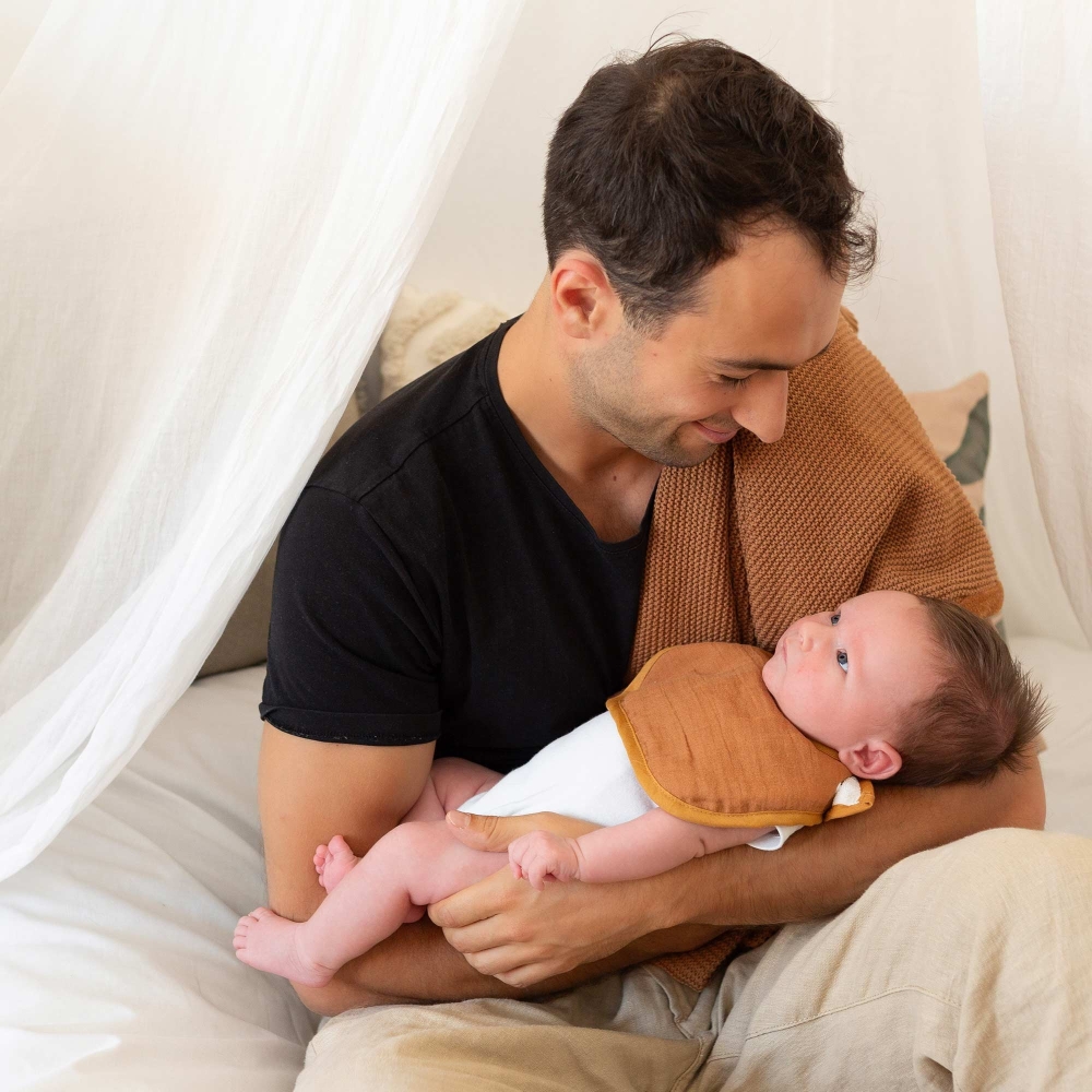 Baby in daddy's arms wearing a terracotta bib Baby in daddy's arms wearing a terracotta bib