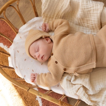 baby sleeping in bassinet with knitted outfit