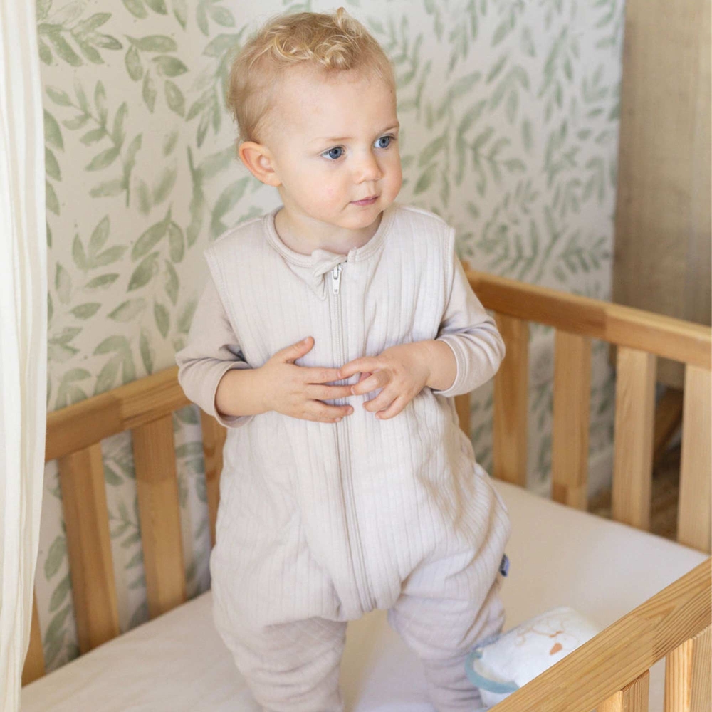 Baby trägt seinen Schlafsack mit Füßen in seinem Bett