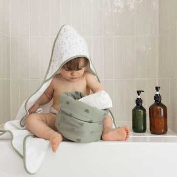 Bebé à saída do banho com a sua toalha de banho com capuz e o seu cesto de produtos de higiene