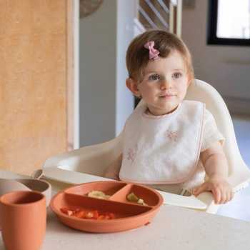 bebé à mesa com o seu babete branco com flores cor-de-rosa bebé à mesa com o seu babete branco com flores cor-de-rosa