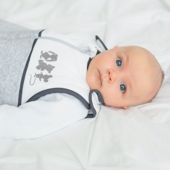 baby boy with blue eyes lying in his bed with his unisex sleep bag