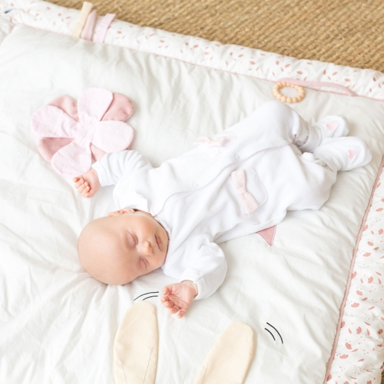 Pink and white play mat with a small baby lying on it