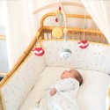 Bebé deitado na cama a olhar para o seu móbile musical, com o resguardo de cama com motivos de bosque