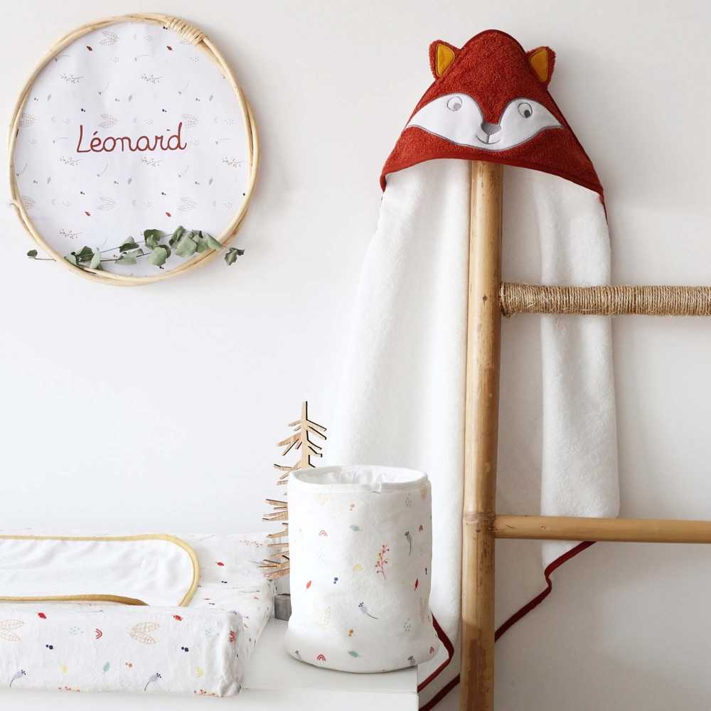 Pequeno saco com produtos para bebé pousado na cómoda, junto à capa de banho com raposa