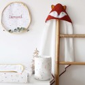 Pequeno saco com produtos para bebé pousado na cómoda, junto à capa de banho com raposa