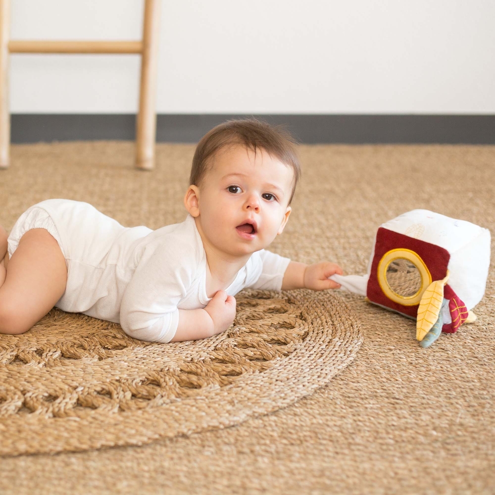 Baby on carpet playing with sensory cube.