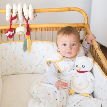 Baby sitting in bed in a sleeping bag with musical soft toy