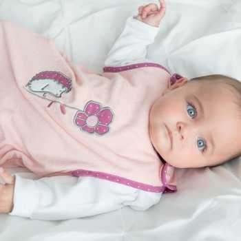 Bebé menina de olhos azuis com o seu saco de dormir de verão rosa salmão