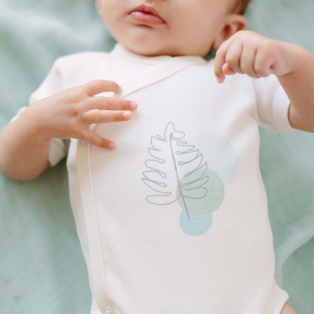Zoom sur le body écru tropical avec les mains de bébé Zoom sur le body écru tropical avec les mains de bébé