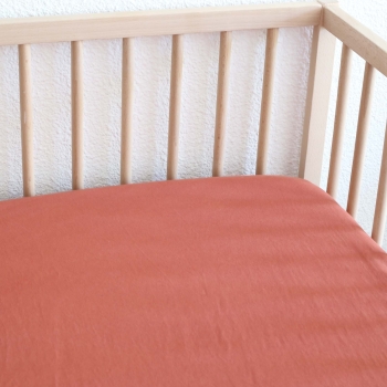 solid terracotta baby fitted sheet in a wooden bed