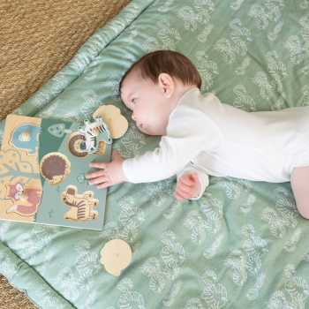 Bebé a brincar com o seu puzzle de madeira no seu tapete de atividades com folhas