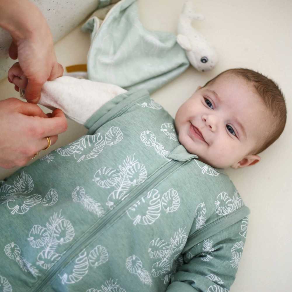 Bebé a sorrir enquanto a mamã lhe desaperta as mangas do seu saco de dormir verde