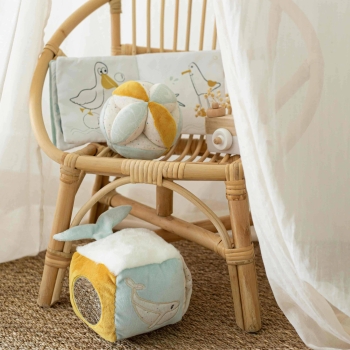 Sensorische kubus op de grond met ander babyspeelgoed uit de collectie op een rieten stoel Sensorische kubus op de grond met ander babyspeelgoed uit de collectie op een rieten stoel