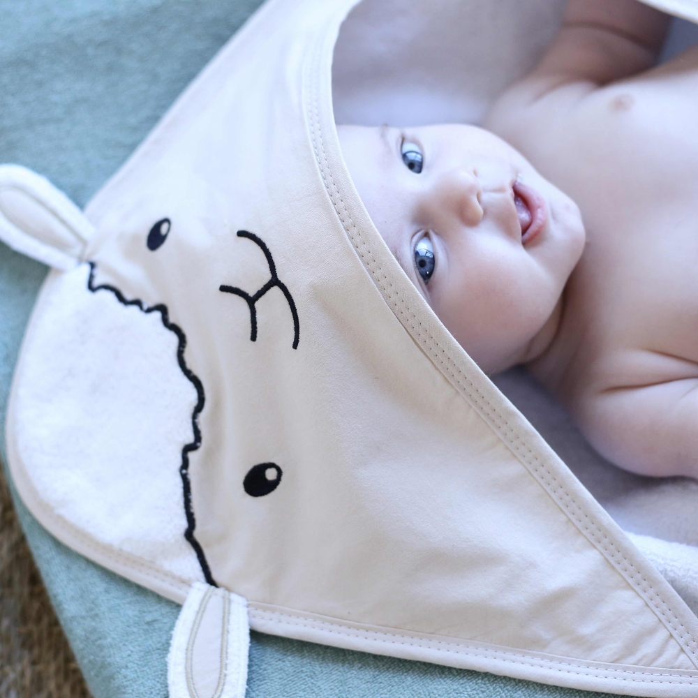 Bebé que se ríe en su capa de baño del bebé decorada pequeña oveja