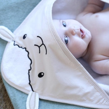 Bebé que se ríe en su capa de baño del bebé decorada pequeña oveja