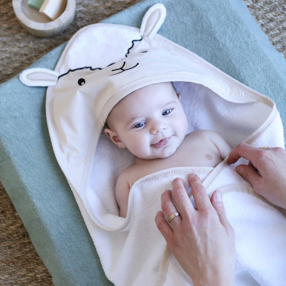 Mamá que seca a su bebé con la capa de baño beige con pequeñas orejas de oveja