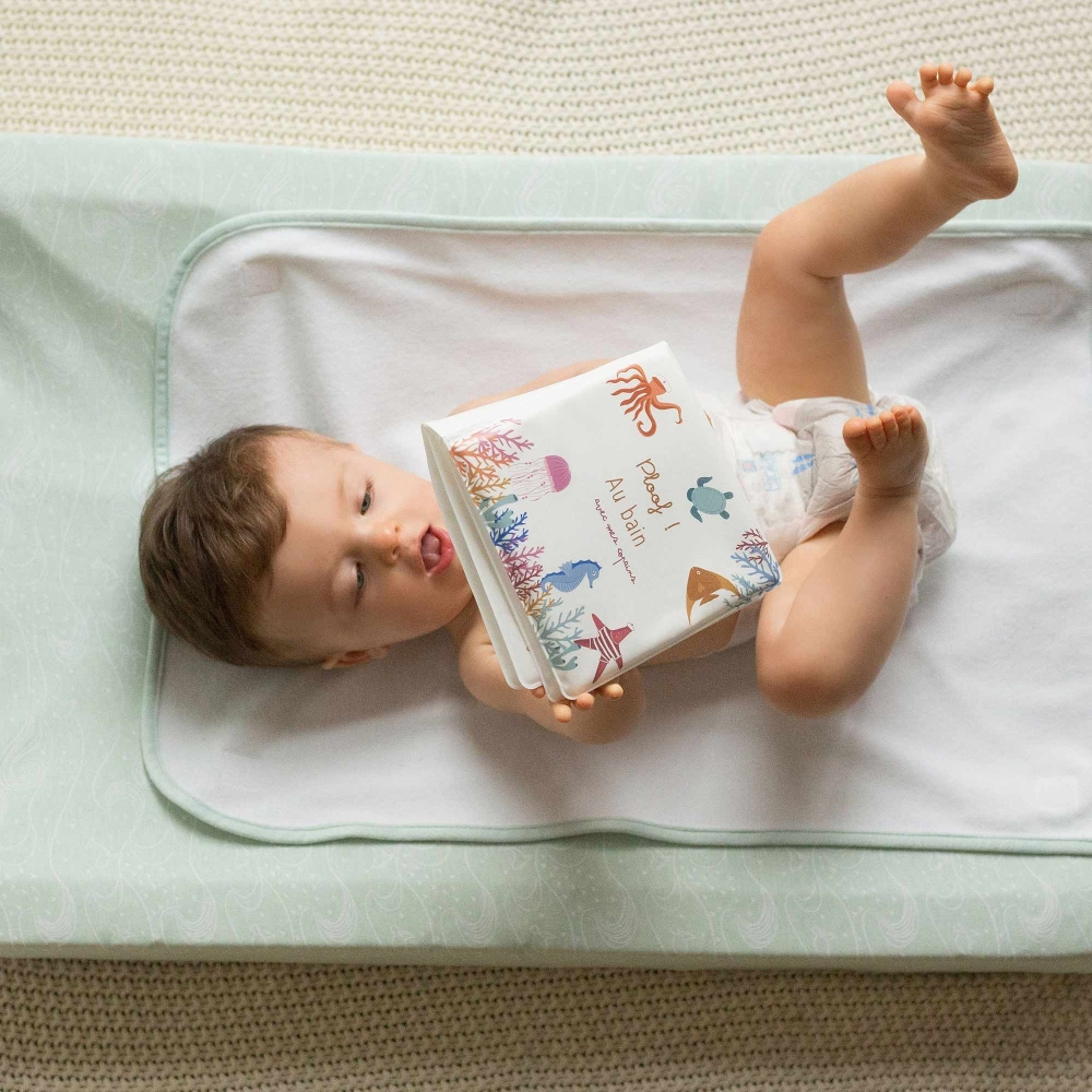Baby playing with bath book laying in diaper on changing mat Baby playing with bath book laying in diaper on changing mat