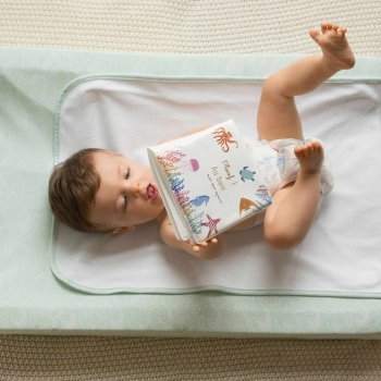 Baby die met zijn badboekje speelt liggend in luier op zijn aankleedkussen Baby die met zijn badboekje speelt liggend in luier op zijn aankleedkussen