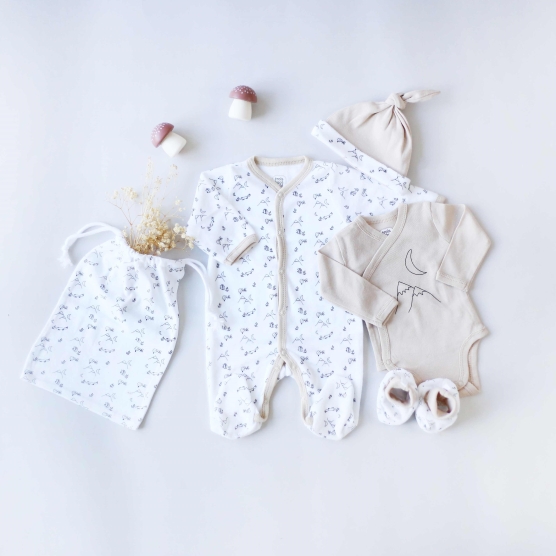 Beige and white newborn set including pajamas, bodysuit, booties, hat and storage bag