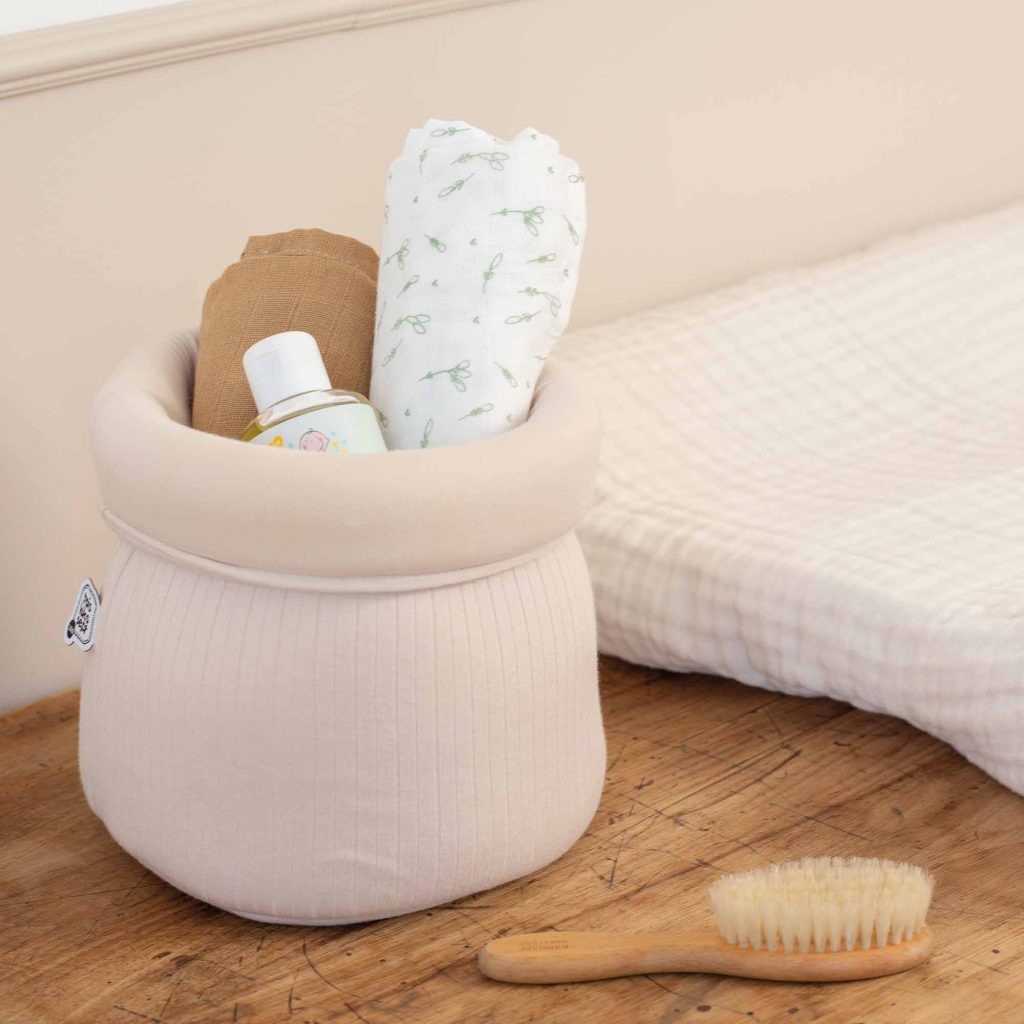 Panière de rangement pour bébé garnie d'un lange camel et d'un lange avec des épis de blés mixtes à côté d'un matelas à langer beige