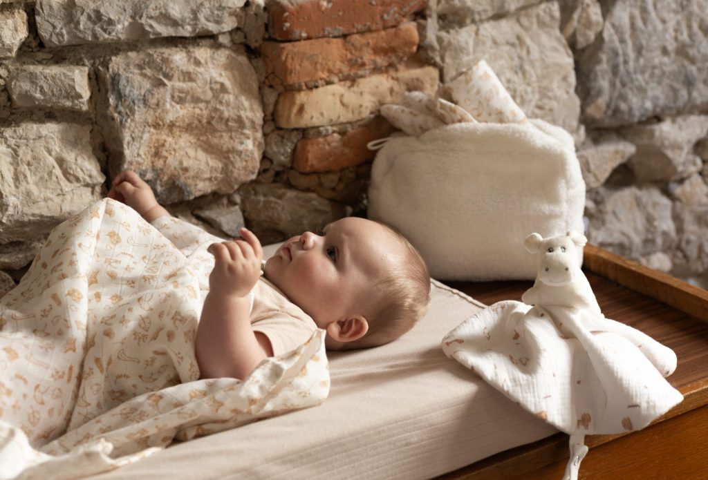 bébé sur son matelas à langer, recouvert d'un lange aux doux motifs de la ferme