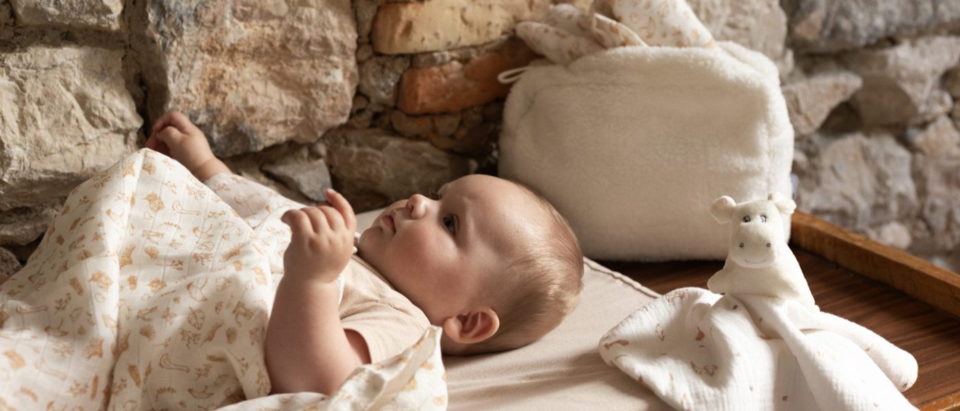 bébé sur son matelas à langer, recouvert d'un lange aux doux motifs de la ferme