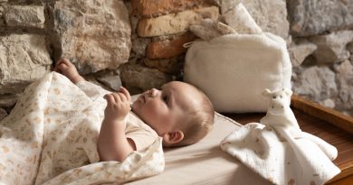bébé sur son matelas à langer, recouvert d'un lange aux doux motifs de la ferme