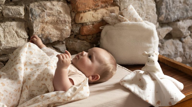 bébé sur son matelas à langer, recouvert d'un lange aux doux motifs de la ferme